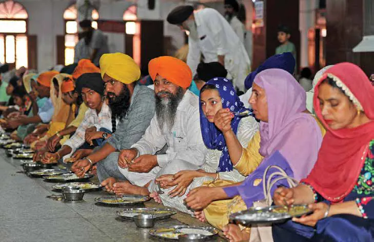 Rows of people seated on the floor being served langar