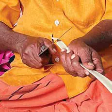 Hands cutting a strip of palm leaf with a blade