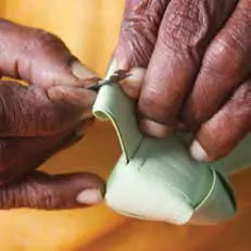 Hands folding palm-leaf strips into a shape