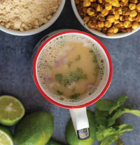 A mug of sattu drink beside bowls of roasted chickpeas and flour