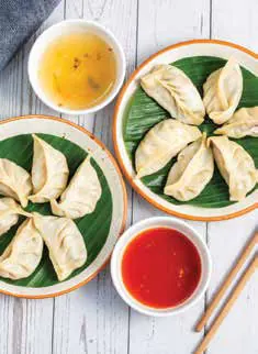 Plates of momos with a bowl of red chutney and soup