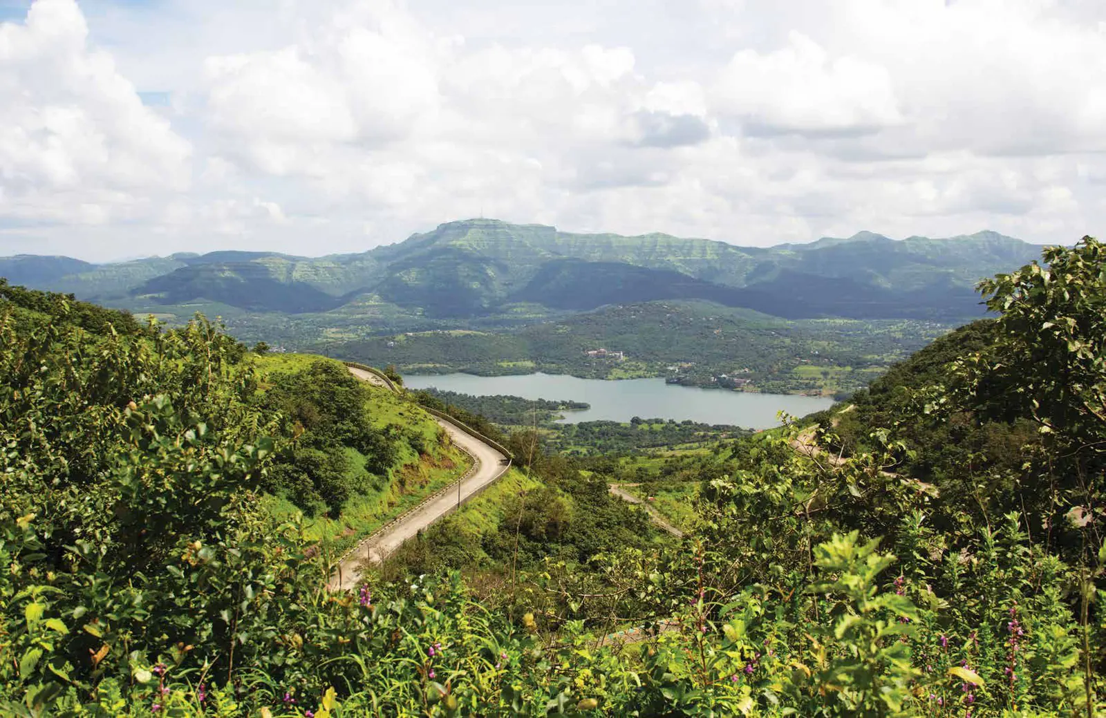 A road winding through green hills above a lake
