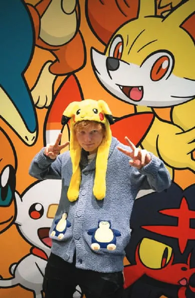 Ed Sheeran in a Pikachu hat against a cartoon mural