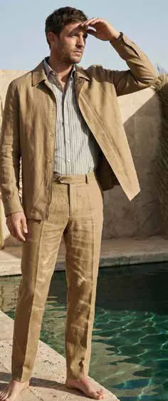 A man in a beige linen suit shading his eyes beside a pool