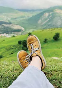 Feet in suede shoes resting on a grassy hillside above a valley