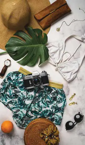 A flat lay of a tropical-print shirt, a straw hat, a camera and accessories