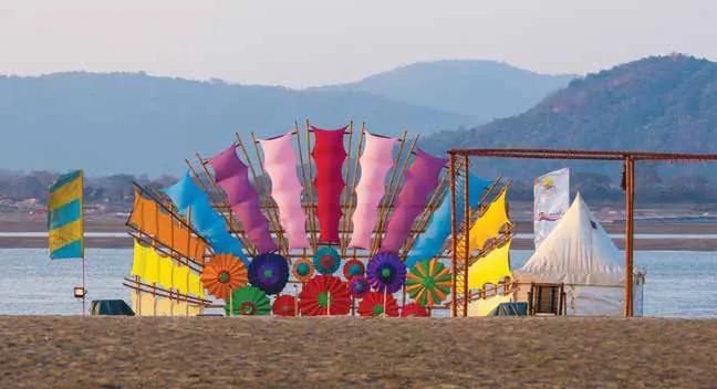 Brightly coloured sail-like panels set up on a sandbank beside a white tent