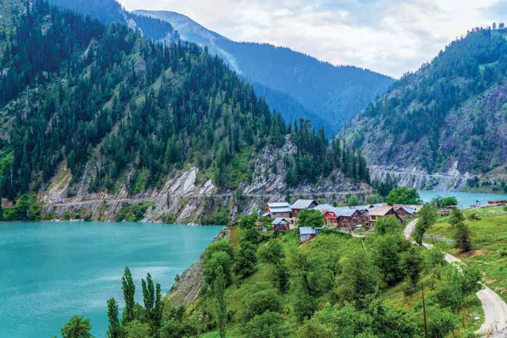 A turquoise lake below forested mountains, with a village of timber houses on the slope