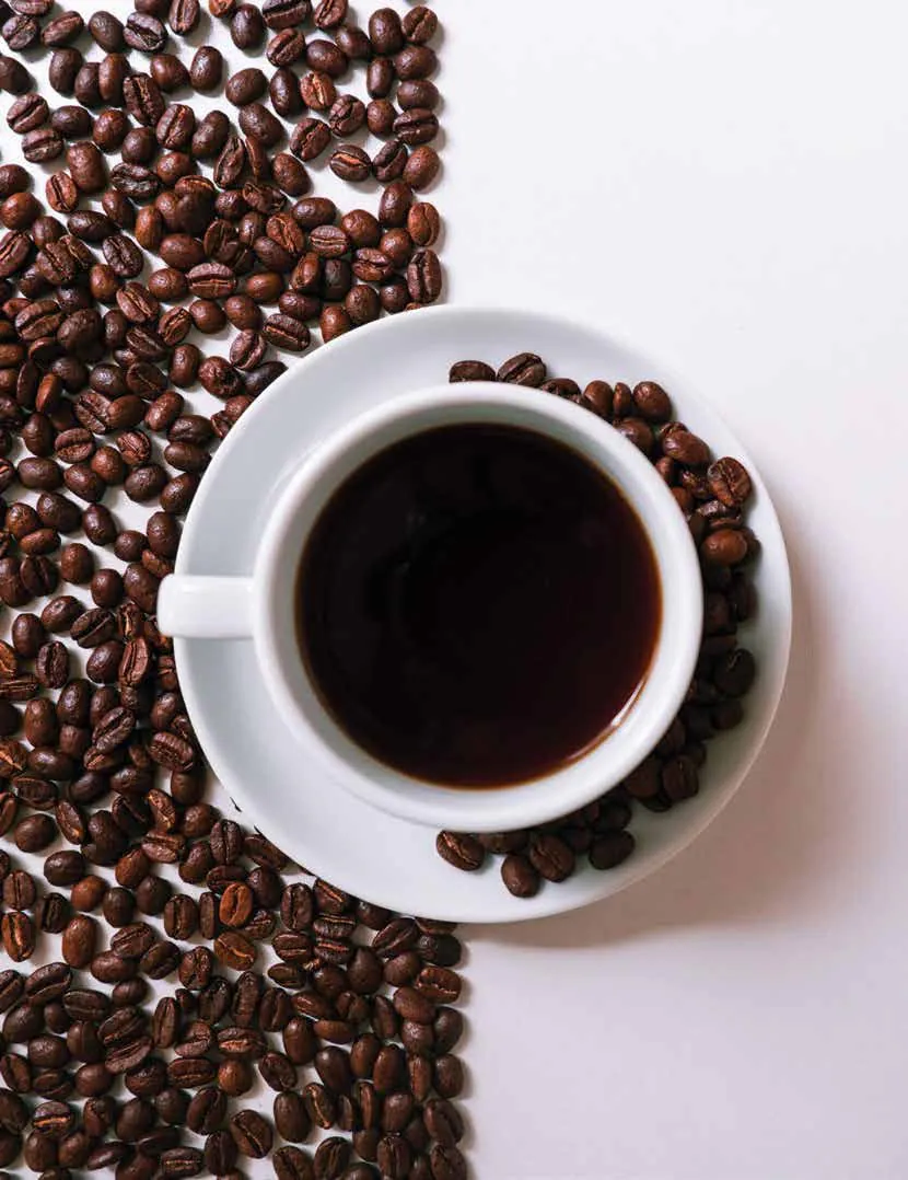 A cup of black coffee on a saucer, surrounded by roasted coffee beans
