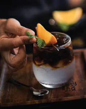 A layered coffee drink garnished with a slice of orange