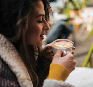 A woman smiling as she holds a cup of coffee