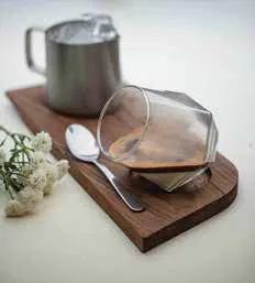 A glass of coffee and a steel jug on a wooden tray