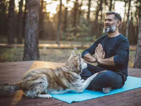 A man meditating on a mat with a cat lying beside him