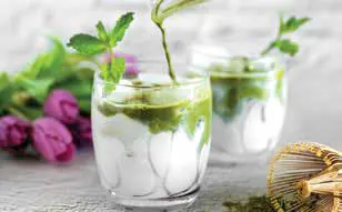 Two glasses of a green drink with fresh herbs