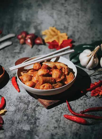 A bowl of a spiced dish with chopsticks and dried chillies