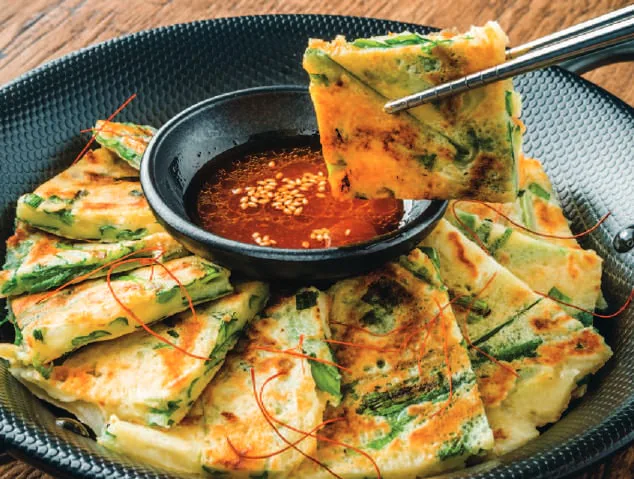 A Korean pancake being dipped in sauce