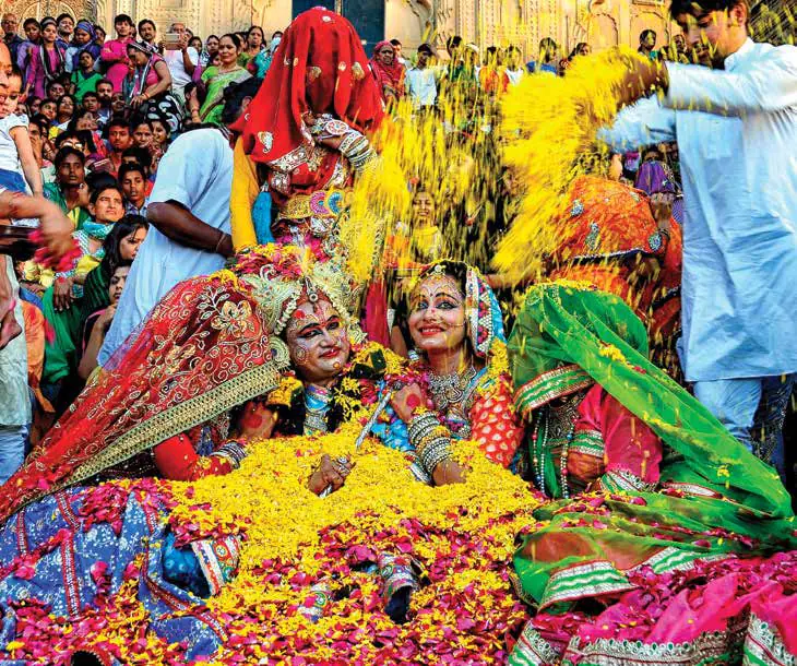 Devotees dressed as Radha and Krishna amid showers of flowers