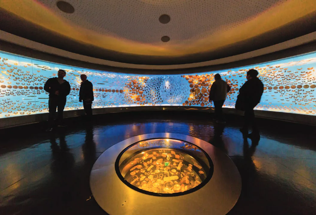 Visitors in a dark gallery around a glowing display of gold