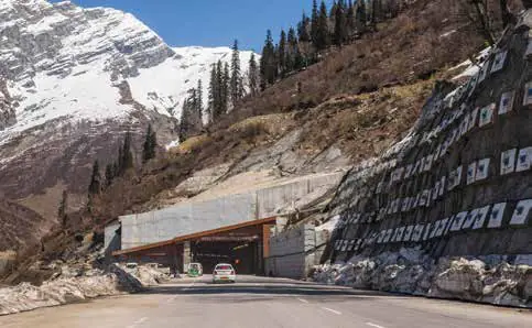 A road leading to a tunnel entrance beneath a snowy mountain slope