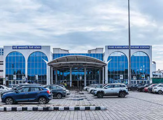 The glass-fronted facade of a railway station with cars parked in front