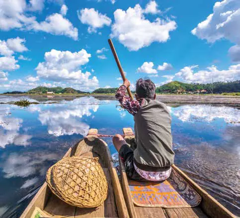 A boatman poling a dinghy across a lake reflecting the clouds