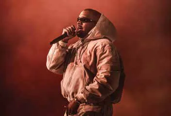 A performer in a hooded jacket singing into a microphone in red light
