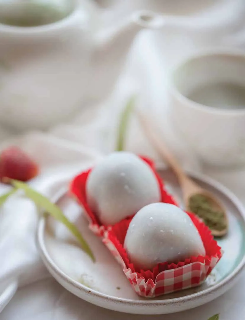 Two white mochi on a small plate beside a teapot