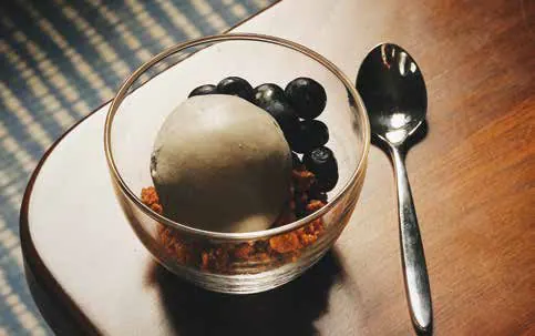 A scoop of dark ice cream in a glass bowl with berries