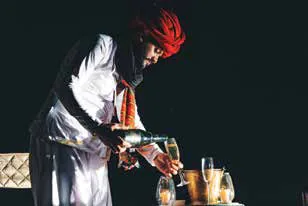 A man in a red turban and white attire pouring a drink