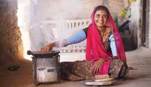 A woman in a pink headscarf cooking at a small stove