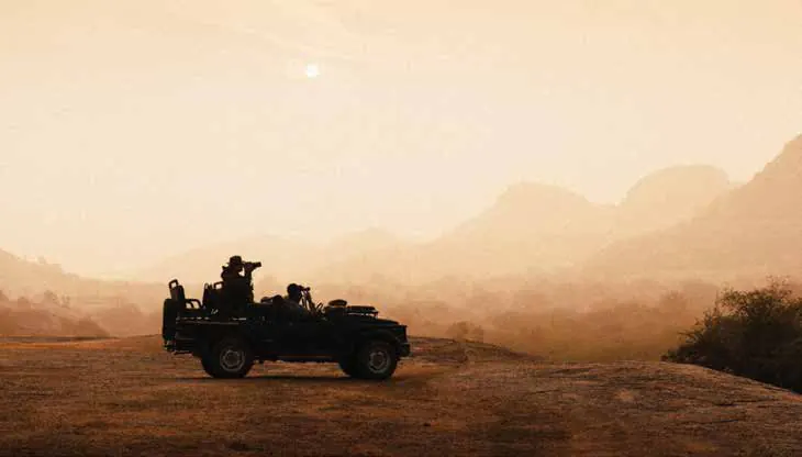 A safari jeep silhouetted on a ridge against hazy hills at sunrise