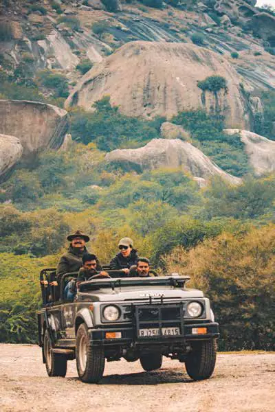 Visitors in an open safari jeep driving through a rocky, wooded landscape