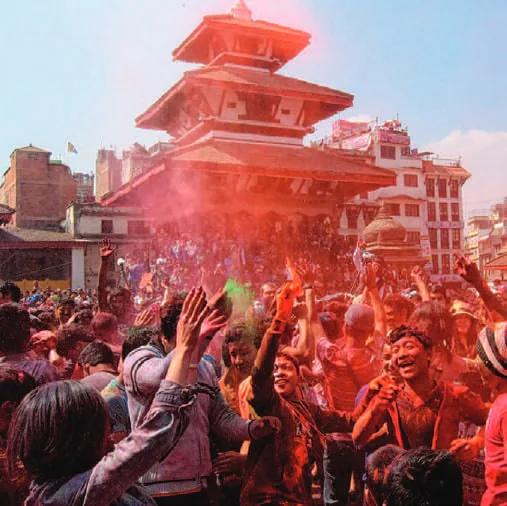 Crowds celebrating Holi in clouds of colour before a pagoda