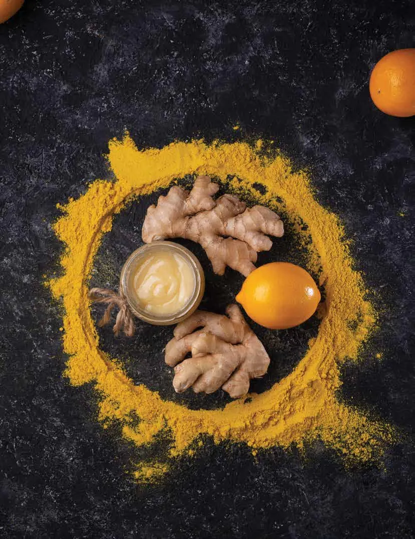 Turmeric powder, turmeric root, fresh ginger and citrus on a dark surface