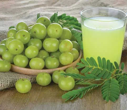 Green amla fruit in a bowl beside a glass of amla juice