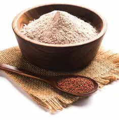 A bowl of millet flour with whole grains on a spoon
