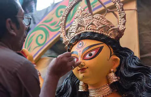 An artisan painting the face of a clay goddess idol