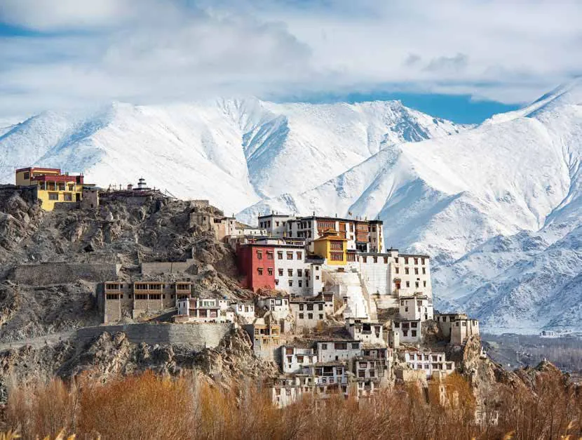A monastery on a rocky hilltop below snow-capped mountains in Ladakh