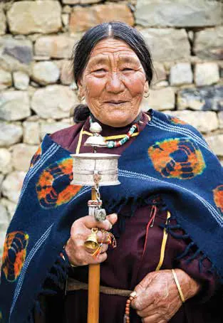 An elderly woman in traditional dress holding a hand prayer wheel