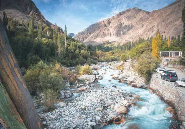 A clear stream running through a rocky valley past trees