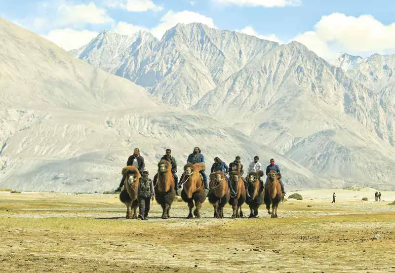 A line of camel riders crossing a sandy valley below mountains
