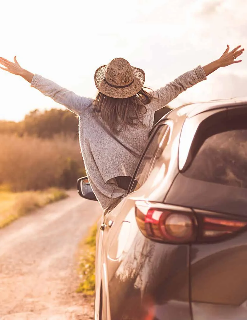A traveller leaning out of a car window with arms outstretched on a country road