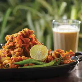A plate of fried pakoras with a glass of tea