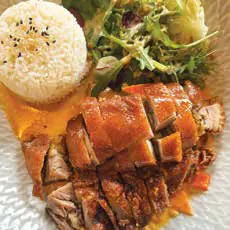 A plate of rice with roast meat and greens