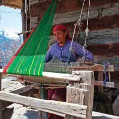 A woman in a headscarf weaving at a wooden loom
