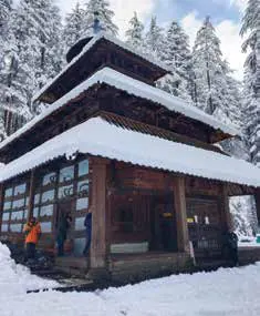 A tiered wooden temple covered in snow among pine trees