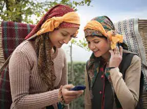 Two young women in headscarves looking at a phone together