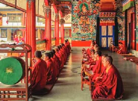 Monks seated in rows inside a colourful monastery hall