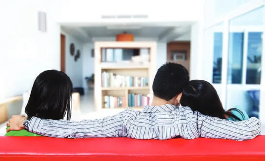 Three people seen from behind, sitting close together on a red sofa