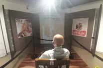 A seated figure in a chair facing a museum corridor lined with exhibits